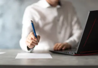 Mężczyzna siedzący przy laptopie i trzymający długopis w ręcę