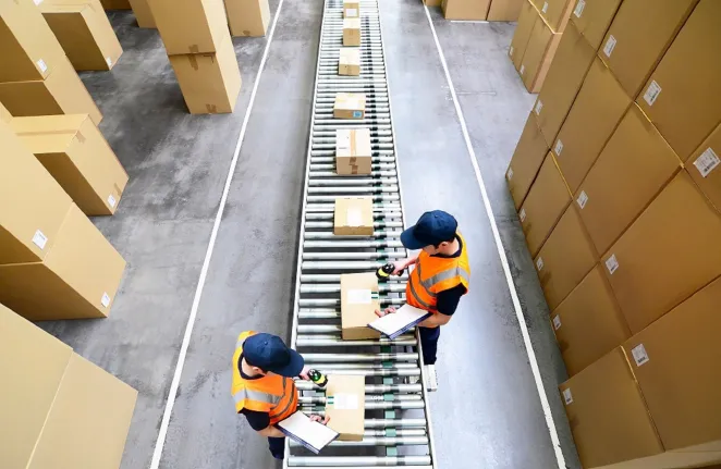 Na zdjęciu znajdują się dwie osoby pracujące przy taśmie produkcyjnej 